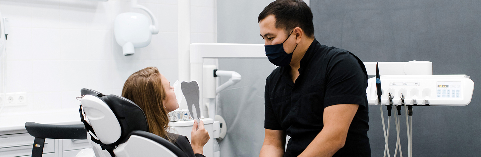 A dentist and patient in an examination room. The patient is looking at her teeth in a mirror.