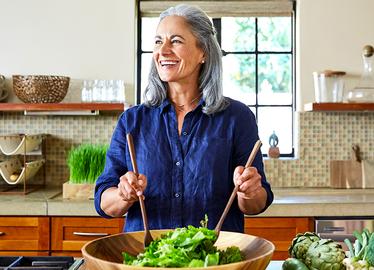 Portrait Of Mature Woman Preparing A Healthy Salad In The Kitchen At Home Laughing