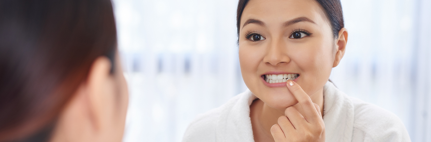 Young woman wearing a robe and examining her teeth in the mirror