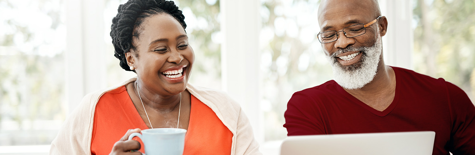 Older attractive couple looking at a laptop and smiling while eating a meal.