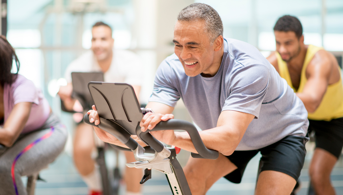 Older man smiling while cycling on an exercise bike at a spin class