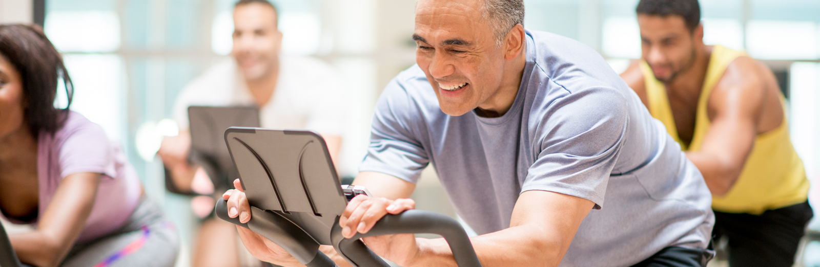 Older man smiling while cycling on an exercise bike at a spin class