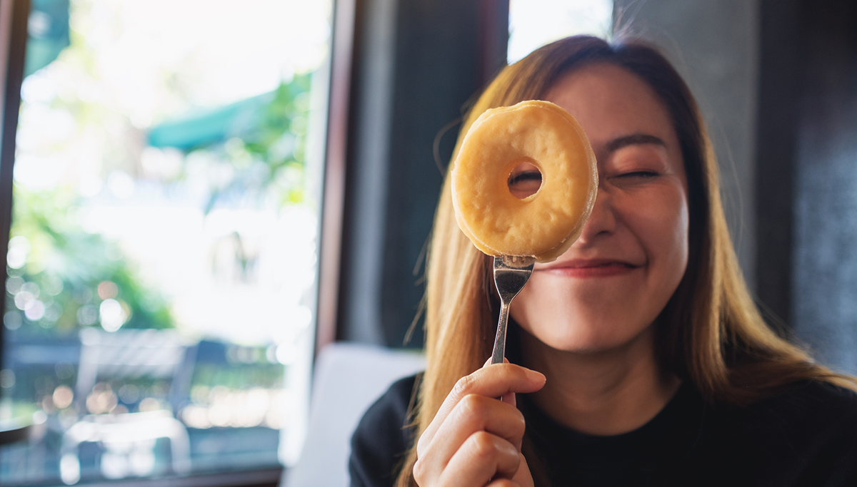 A funny young woman cover her eye and looking through donut