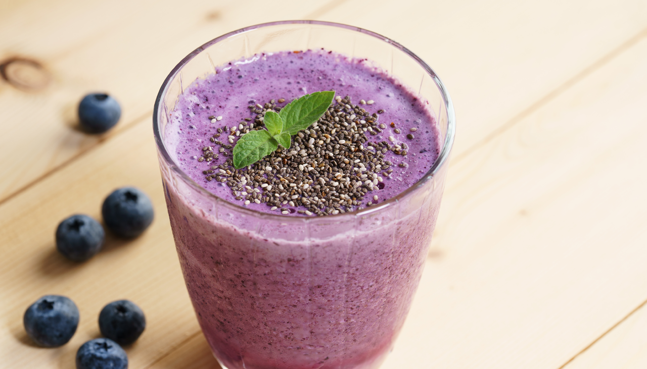 closeup of a glass full of blueberry smoothie on a wood table