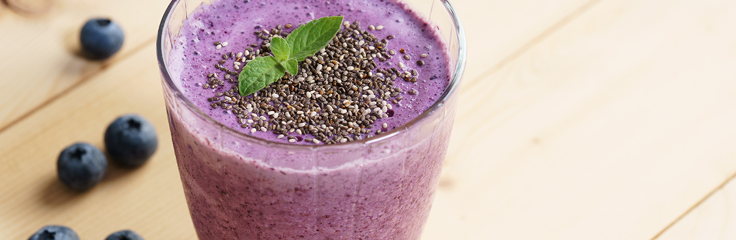 closeup of a glass full of blueberry smoothie on a wood table