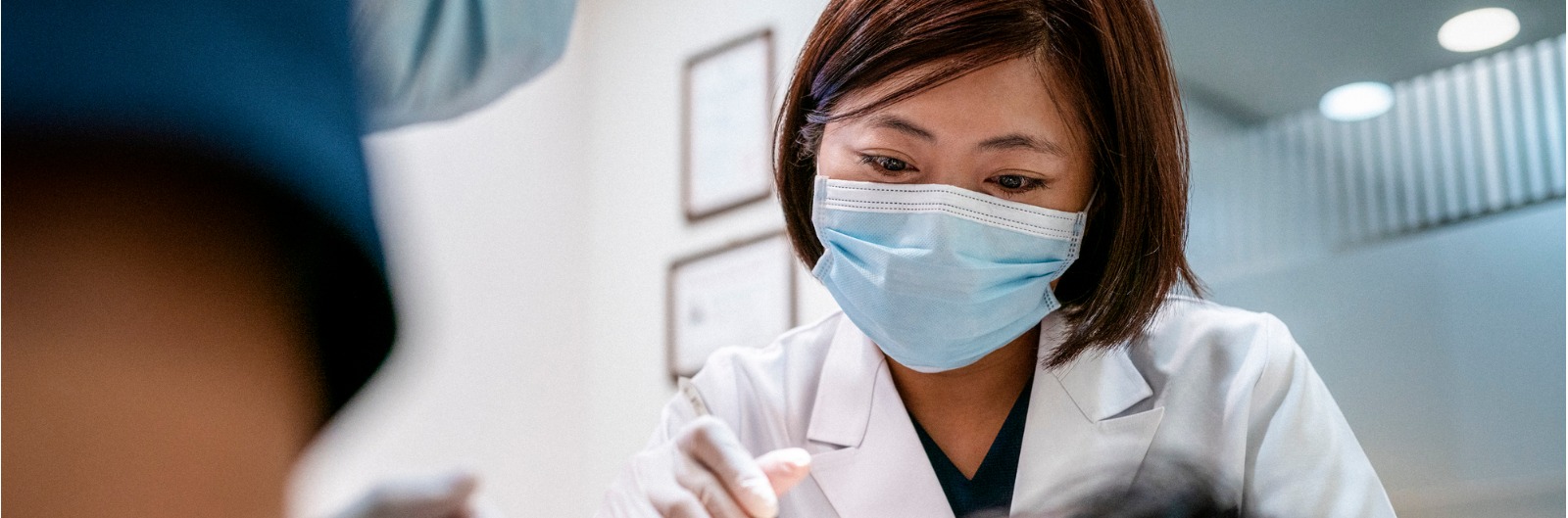 Dentist and her assistant wearing blue face masks examine a patient