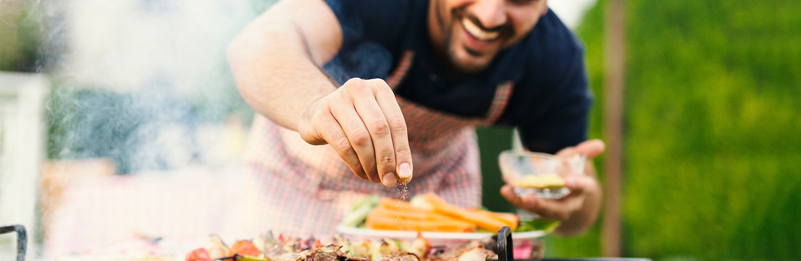 Smiling man seasoning food on an outdoor grill