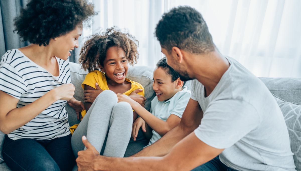 1200x683_Young family with a mom dad and two children sit on a couch at home smiling and talking