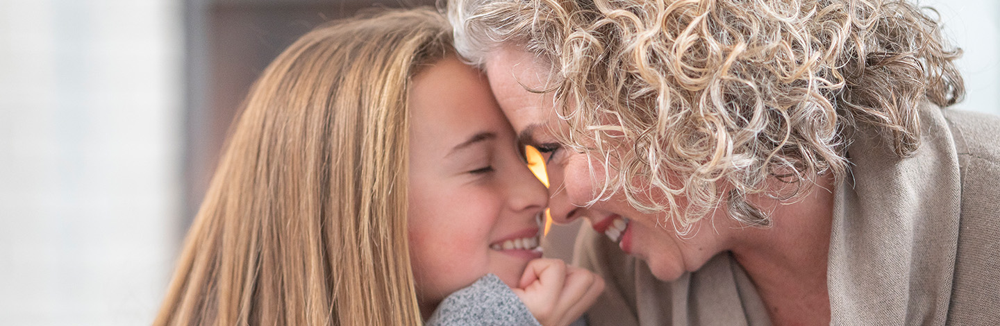 young girl and older woman smile while leaning in close to one another touching foreheads