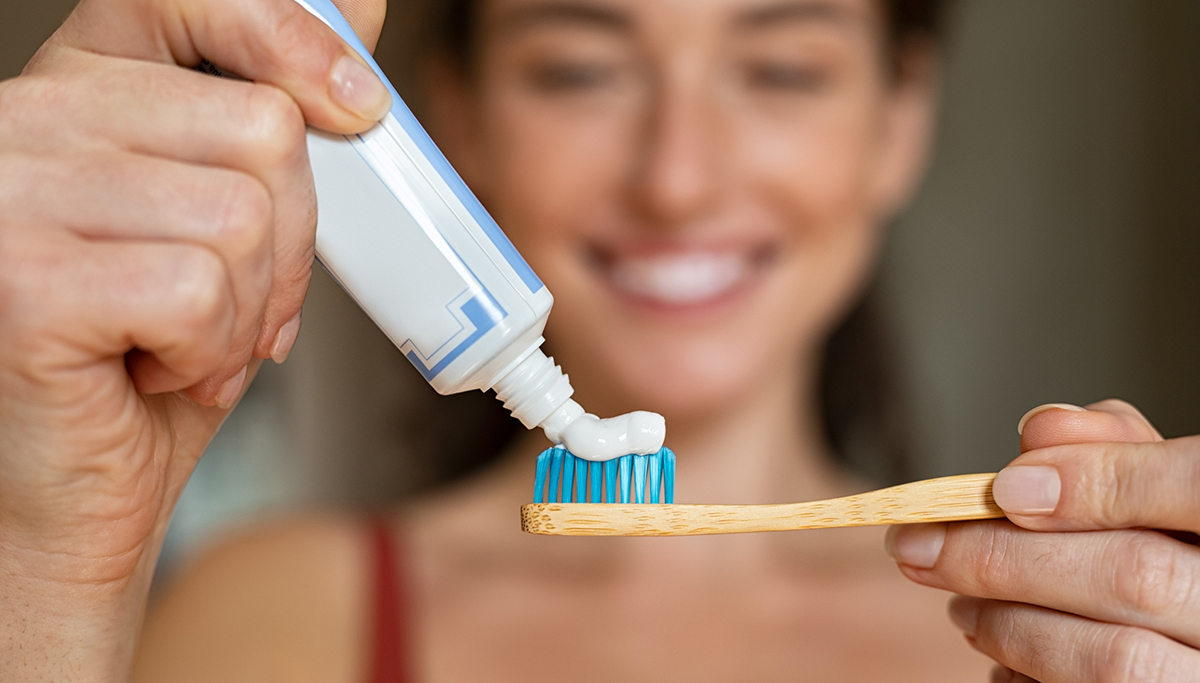 Close up of woman with tooth brush applying paste in bathroom. Closeup of girl hands squeezing toothpaste on ecological wooden brush. Smiling beautiful woman applying toothpaste on eco friendly toothbrush.