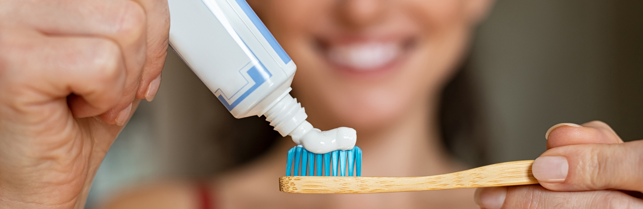 Close up of woman with tooth brush applying paste in bathroom. Closeup of girl hands squeezing toothpaste on ecological wooden brush. Smiling beautiful woman applying toothpaste on eco friendly toothbrush.
