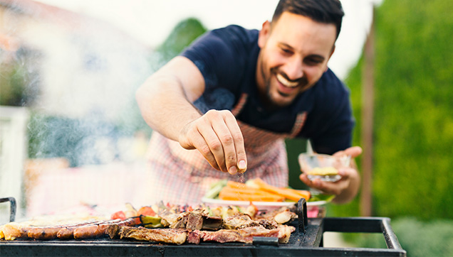 Smiling man seasoning food on an outdoor grill