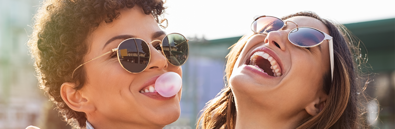 Two women with sunglasses outside in the sun smiling and laughing